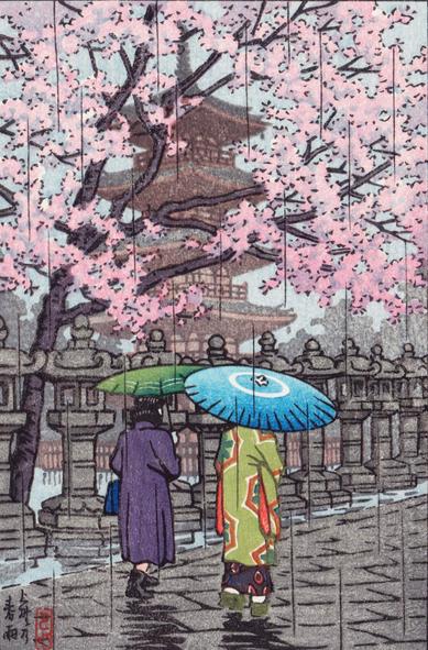 A light rain falls on a spring day in Ueno Park. A pair of visitors to the park carry bamboo umbrellas as they walk beneath cherry trees in full bloom. To their left, a row of stone lanterns lines the path, and beyond, the five-story pagoda that was once part of Kaneji Temple stands tall.