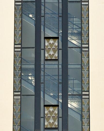 Photo d'une verrière avec des motifs géométriques triangulaires. Derrière on devine un escalier.