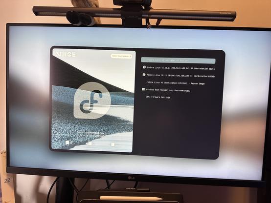 A computer monitor displays a boot menu for Fedora Linux and Windows Boot Manager, featuring options to select various Fedora versions and UEFI firmware settings. The background includes a serene landscape design.