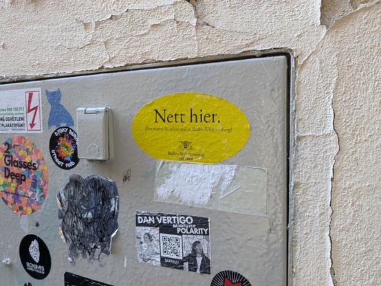 A Nett Hier sticker on a metal door, with other stickers around it