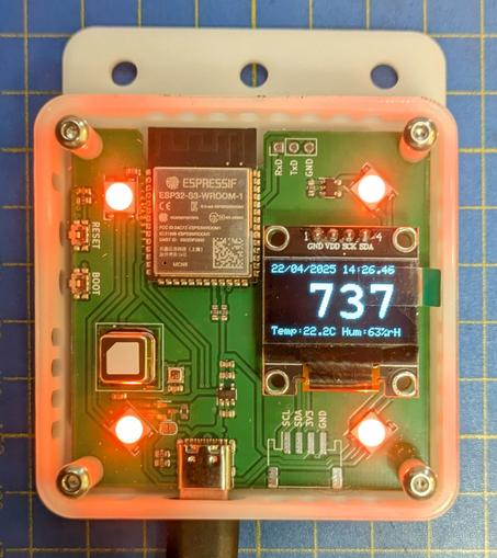 One co2 monitor in a 3d printed white case with a transparent acrylic front panel. The 4 leds (one in each corner) are lit up orange and the display shows 737ppm.