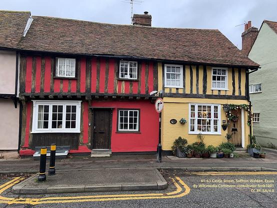 Photo: Two old, two-storey, half-timbered cottages at the right end of a terrace. The cottage on the left is painted in a dark red colour, the one on the right a yellowish colour.