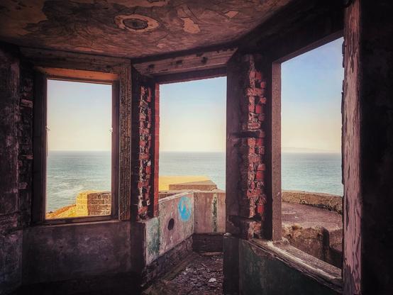 Interior view of a dilapidated structure with open windows framing the ocean.