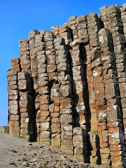 A close-up view of the hexagonal basalt columns forming the Giant's Causeway under a clear blue sky. The textured grey and brown stones create a unique geometric pattern.