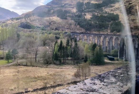 The Glenfinnan Viaduct as seen from a train. It is a curved bridge comprised of stone arches.
