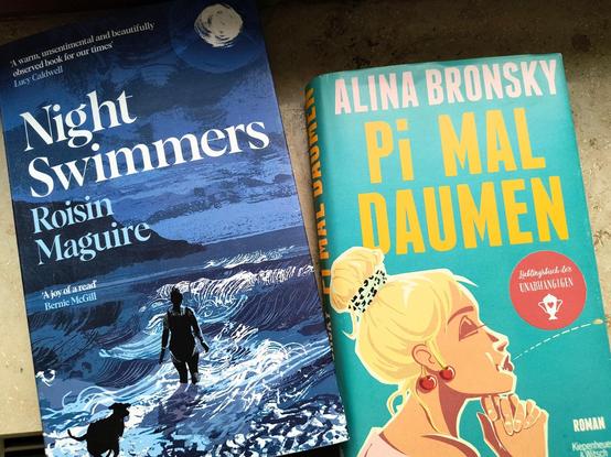 Zwei Buchcover, "Night Swimmers" von der Irin Roisin Maguire und "Pi mal Daumen" von der Berliner Autorin Alina Bronsky. Auf dem Cover von "Night Swimmers" ist eine Illustration einer nächtlichen, in dunkelblauen Schattierungen gemalten Szene am Meer zu sehen, in der eine Frau im Badeanzug mit einem Hund in den Wellen steht. Auf dem Cover von "Pi mal Daumen" ist eine Illustration einer blonden Frau mit einem Dutt  und auffälligen Ohrringen auf einem türkisfarbenen Hintergrund zu sehen.

Two book covers, "Night Swimmers" by Irish author Roisin Maguire and "Pi mal Daumen" by Berlin author Alina Bronsky. The cover of "Night Swimmers" features an illustration of a nocturnal scene by the sea, painted in shades of dark blue, in which a woman in a swimming costume stands in the waves with a dog. The cover of "Pi mal Daumen" features an illustration of a blonde woman with a bun and eye-catching earrings on a turquoise-coloured background.