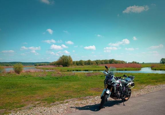 a motorbike parking at a small road. in the background are meadows and a river