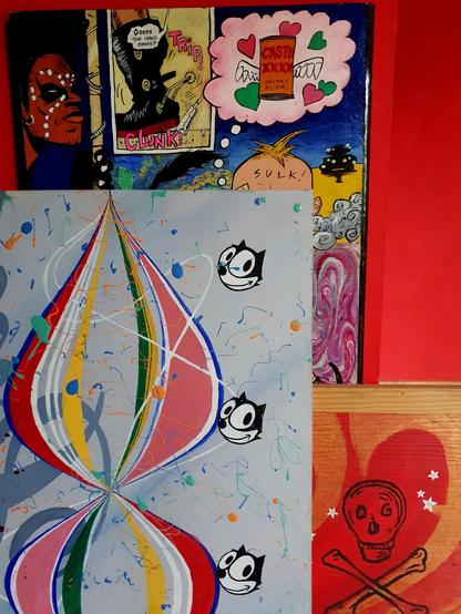 Three colourful paintings by jill strong leaning against a bright red wall