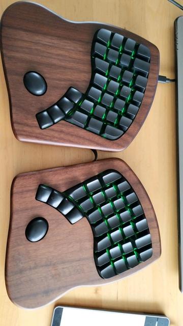 a walnut keyboard.io model 100 with blank black keycaps and sombre green led light