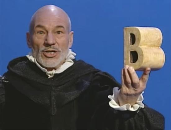 Patrick Stewart in a Shakespearean outfit holding the letter 'b'