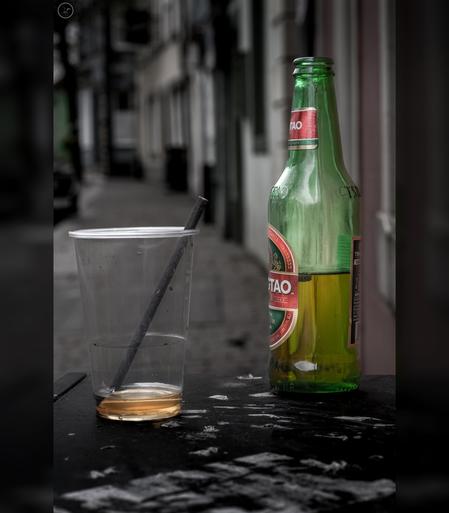 Half drunk beer bottle and plastic cup left on street