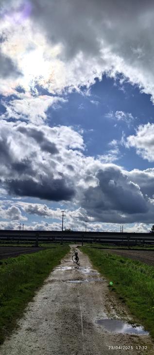 Rail de l'aérotrain au loin avec une masse nuagueuse au dessus. Un train passe en arrière plan.