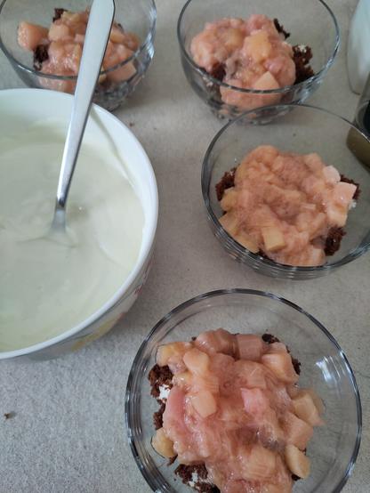 Das Dessert wird zusammen gebaut. Die Kuchenschicht und das Rhabarberkompott wurde bereits verteilt. darauf kommt nun der Joghurt.