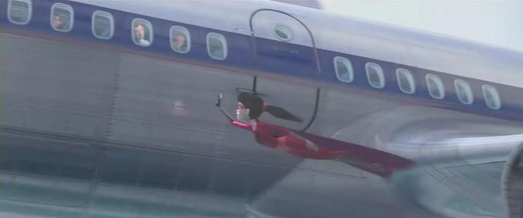 A young superhero girl in a red uniform with a long cape is flying beside an airplane, waving to the people inside.
