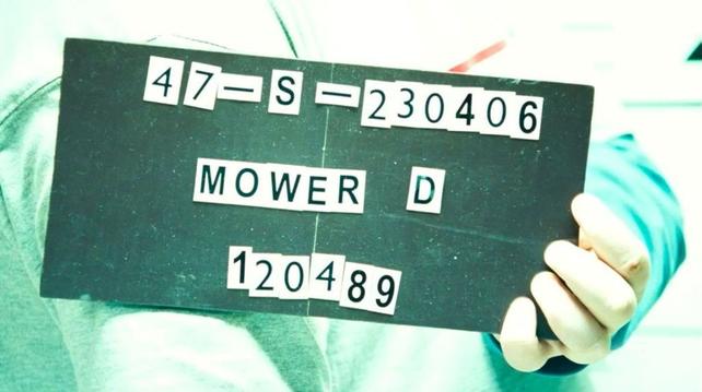 A close-up of a sign being held by a teen who is having his booking photo taken at a police station. The date reads “23-04-06”