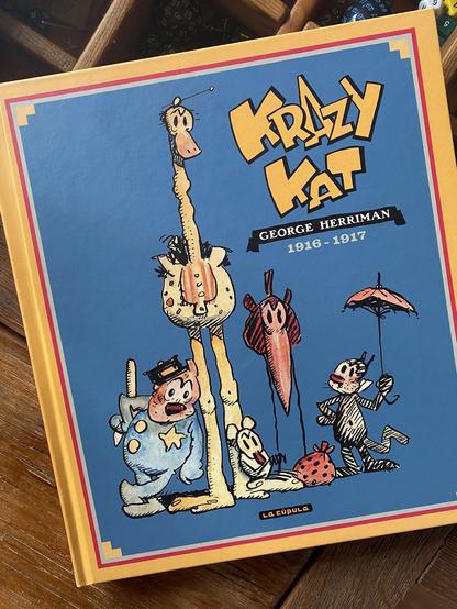 Portada del tomo recopiltatorio de las tiras de Krazy Kat de los años 1916 y 1917. La portada son diferentes personajes estilo cartoon: un perro policía, un pájaro gigante, el ratón Ignatz, un pájaro con un pico inmenso y el gato Krazy Kat debajo de un paraguas.