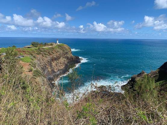 A lighthouse sits atop a tall spit of land over the Pacific Ocean on a very pleasant day.