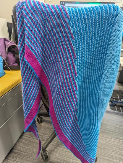 A colorful shawl hanging on an office chair.

The shawl is stripes of light blue, medium blue, and a deep pink (almost magenta). It has long skinny tails and hangs down nearly to the ground.