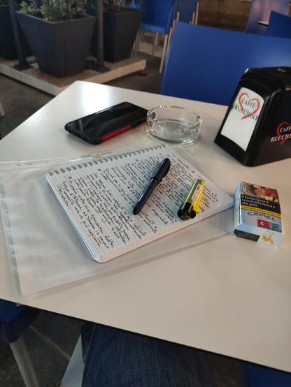 Tavolino con quaderno scritto, penna, accendino, sigarette camel e smartphone