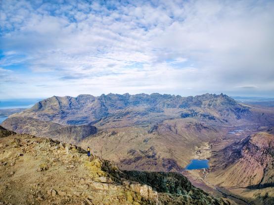 An image of a mountain top looking towards more mountains under a blue sky. Isle of Skye, Scotland