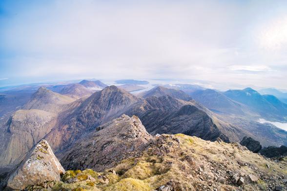 An image of a mountain top looking towards more mountains under a blue sky. Isle of Skye, Scotland