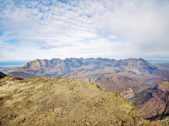 An image of a mountain top looking towards more mountains under a blue sky. Isle of Skye, Scotland