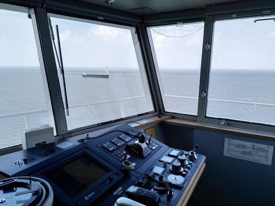 Im Vordergrund: Konsole einer Schiffsbrücke, Im Brückenfenster in der Ferne: ein Schiff mit Flattnerrotor
