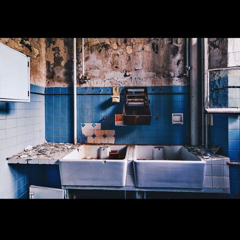 In an abandoned sanatorium, a bathroom with 2 white sinks and an empty hand dryer, with beautiful blue tiles
Photo in color