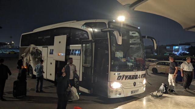 A small travel bus at a bus terminal at night time.