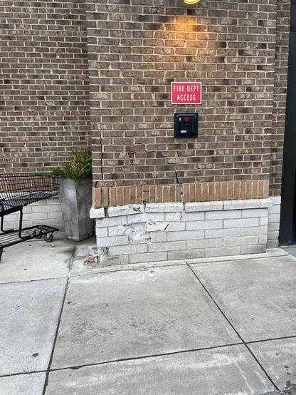 The brick wall of a grocery store, near the entrance, where a motor vehicle hit it and damaged it.