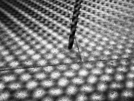 Black and white photo of a chair leg through the metal grill of a chair seat. I probably should have taken the nice white clouds in the sky instead or something. Maybe a cloud photo day tomorrow.
