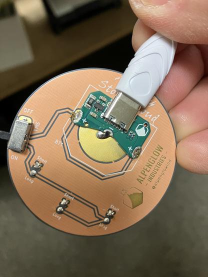 The back of a copper-colored board with a 3V Coin Cell Be Gone soldered in place of a coin cell battery holder, and a USB cable plugged in.