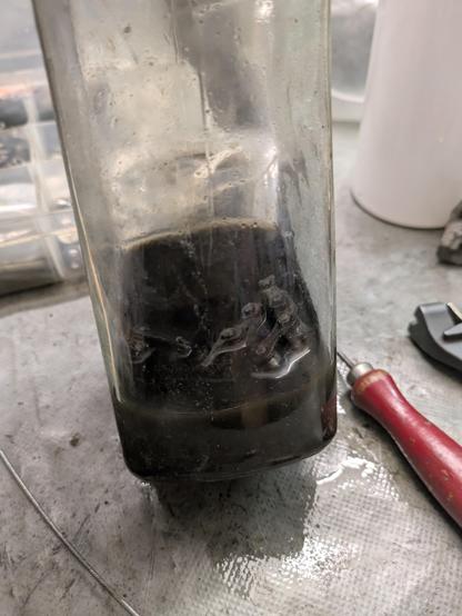 A glass jahr with a black liquid, with a few biycle chain links poking out of the liquid.