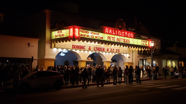 An evening shot (taken from across the street, at around 9:20 pm) of downtown Santa Barbara's Arlington Theatre. There is a crowd of people standing by the entrance, slowly dispersing after the end of an event there. Featured prominently in red neon on the glowing marquee above them is the name "Pete Buttigieg" and "Tuesday 7:30 pm". Also, at the far left of the marquee are the words "Premier Sponsor: Sara Miller McCune".