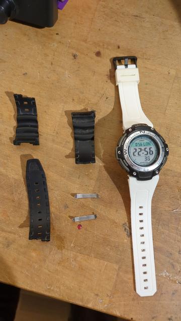 A casio watch with white printed strap on a wooden bench. On the side old strap pieces displayed.