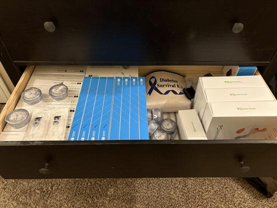 Photo of an open drawer filled with diabetic supplies from Tandem and Dexcom. Most of the drawer on the left side is primarily Tandem supplies for a Mobi insulin pump. On the right are boxes with Dexcom G6 sensors.