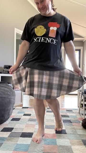 Me doing a kind of cute half-curtsey wearing a dark grey top and pastel pink and grey plaid skirt. The top has a cute minimalist geometrical impression of The Muppets scientists Bunsen and Beaker and the word SCIENCE on it in all caps and clear white bold font.