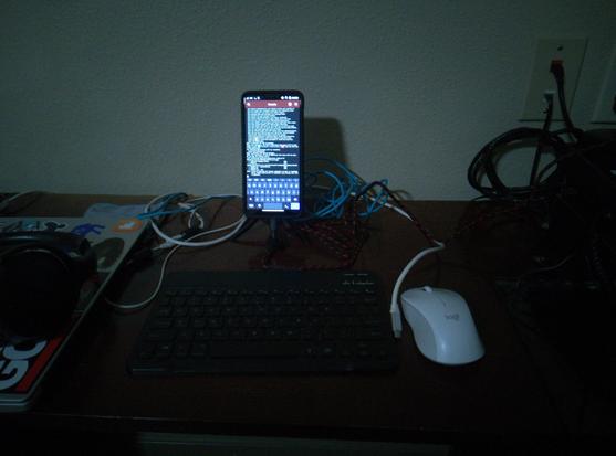 A desk with a mobile phone on a stand, a bluetooth keyboard, mouse.  The phone is presently installing LaTeX.