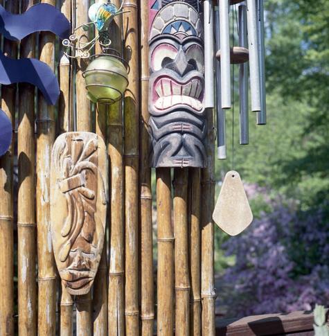 weathered tiki masks and windchime on bamboo fence