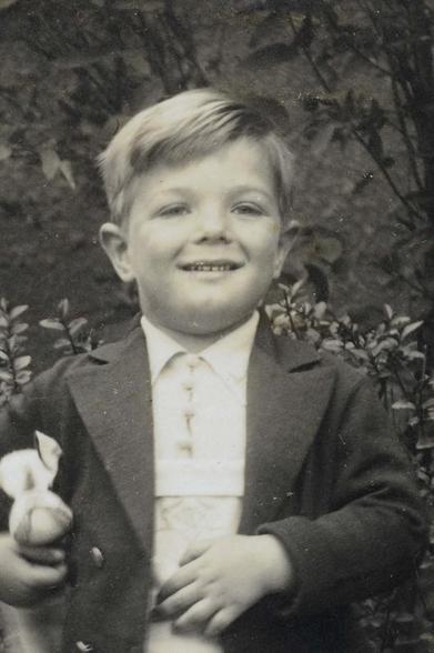 A smiling boy in a tuxedo holding a toy-rabbit.