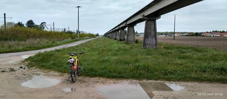 Une randonneuse jaune gentiane est stationnée à proximité du rail de l'aérotrain.
En arrière plan la ville de Cercottes, à droite un chemin de calcaire en direction de la forêt.