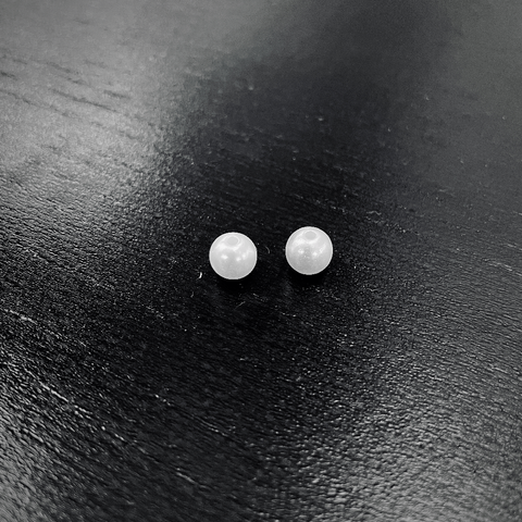 Two small, shiny white beads, pearls perhaps, resting on a dark wooden surface of a table, reflecting light softly.