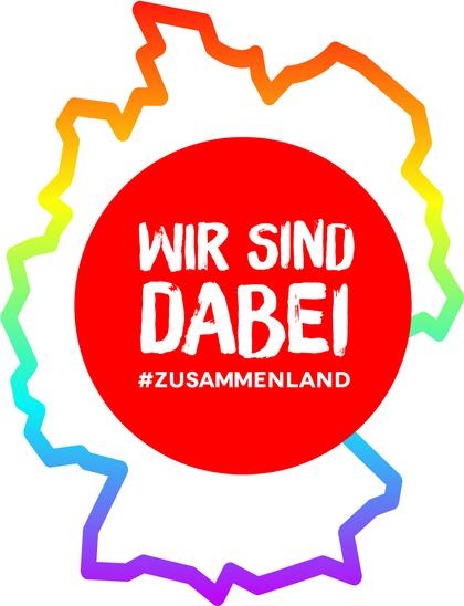 Eine Deutschlandkarte, der Umriss ist in Regebenbogenfarben gestaltet. Darauf ein roter Kreis mit der Aufschrift: Wir sind dabei. Hashtag Zusammenland.