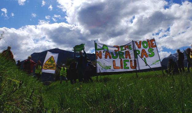 Manifestant⋅es en bord de route devant une banderole "La 3ème voie n'aura pas lieu !"