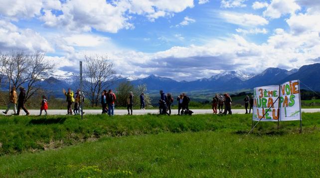 Manifestant⋅es marchant en bord de route devant une banderole "La 3ème voie n'aura pas lieu !"