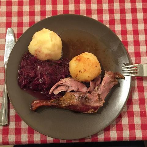 "This picture shows a meal on a dining table, featuring cooked meat, mashed potatoes, red cabbage, and a dumpling topped with gravy. The food is presented neatly on a plate, suggesting it might be a traditional or home-cooked meal."