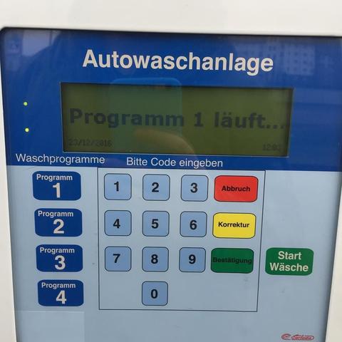 This picture shows a parking meter with various options displayed on its screen. The meter has buttons for payment and a display screen showing the program number, current status (waschprogramm 1 lauf), and possibly other information that is not fully visible or legible due to angle and distance. There are also foreign characters indicating instructions or settings, suggesting an interface designed for users who might not be fluent in the local language. The presence of a credit card machine nearby suggests this is located within a parking facility where payments can be processed electronically. The overall mood or intention of the picture seems to be related to technology and the use of electronic payment systems in urban environments.