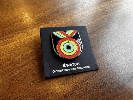 A U-shaped pin badge depicting a medal in the style of Apple’s three activity rings, on a black backing card which reads
“ WATCH Global Close Your Rings Day.”