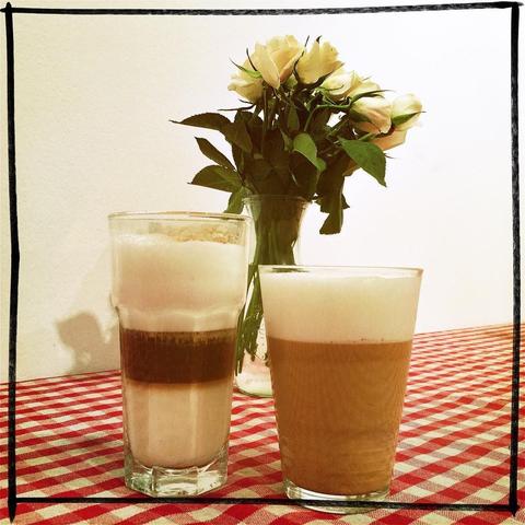 "Two glasses of coffee with latte art on a dining table, framed by white flowers."