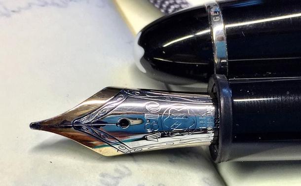 "A pen displaying intricate, colorful designs. The main focus of the image is the pen's detailed craftsmanship. The nib is from a Montblanc Masterpiece fountain pen"